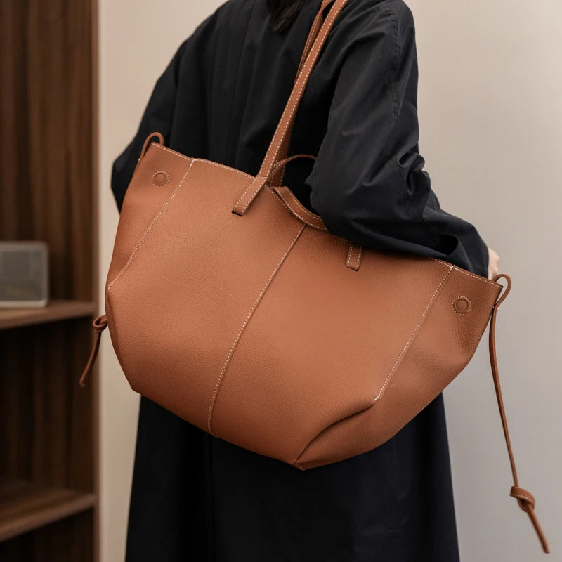 Person holding a brown leather tote bag against a neutral background