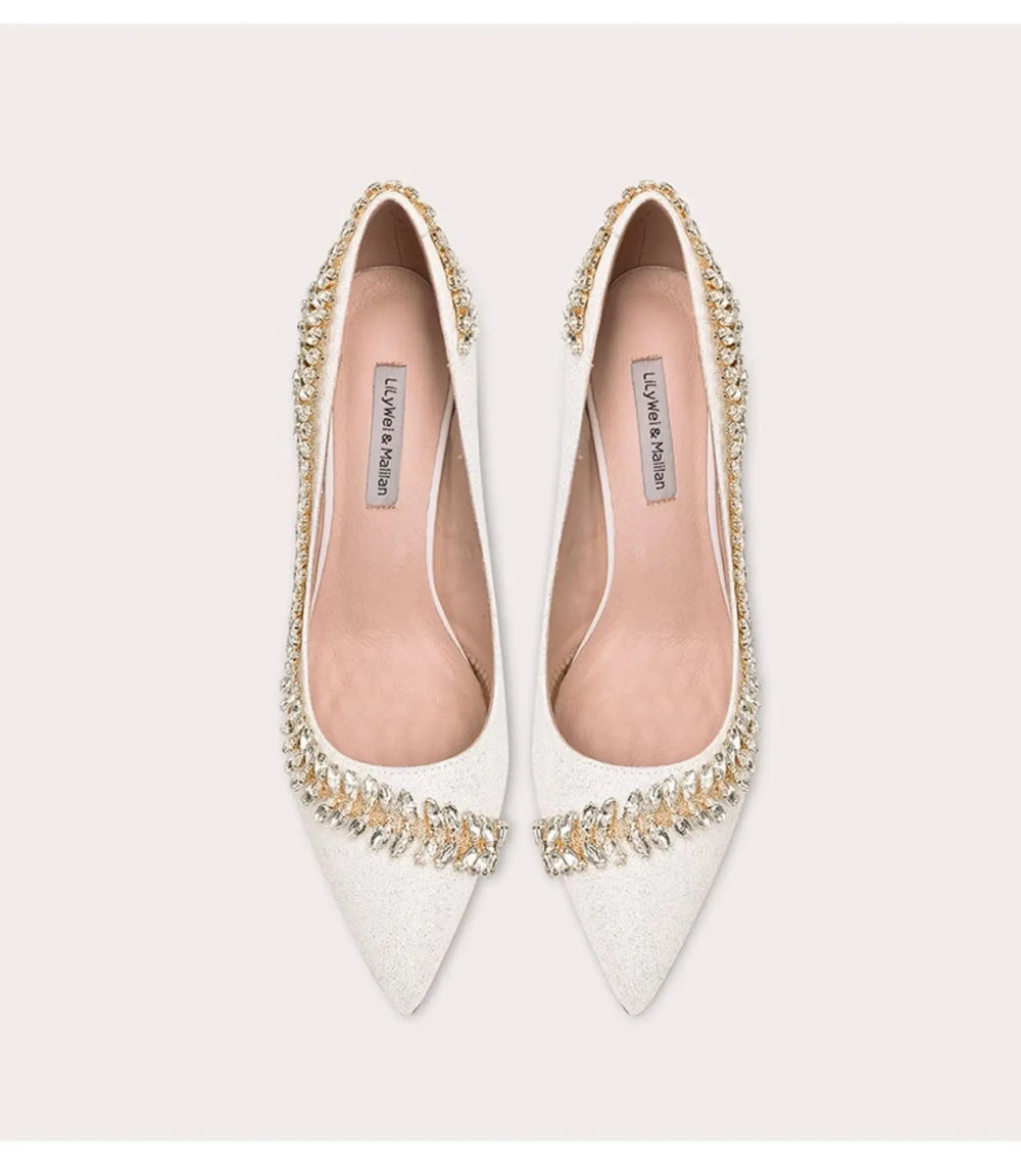 White pointed-toe shoes with embellishments on a light gray background