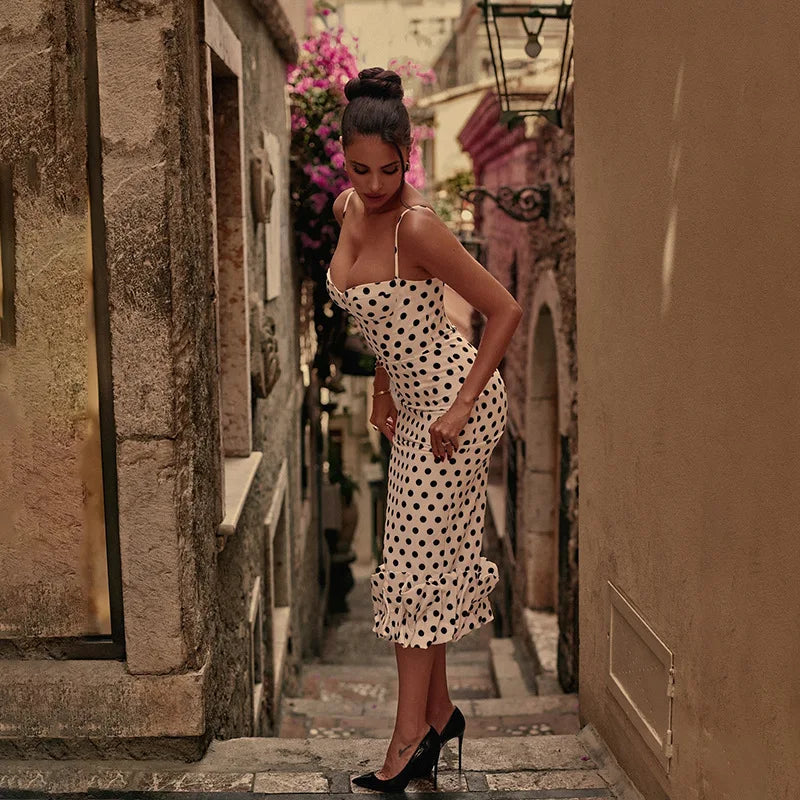Woman in a polka dot dress standing in a narrow alleyway with stone walls.