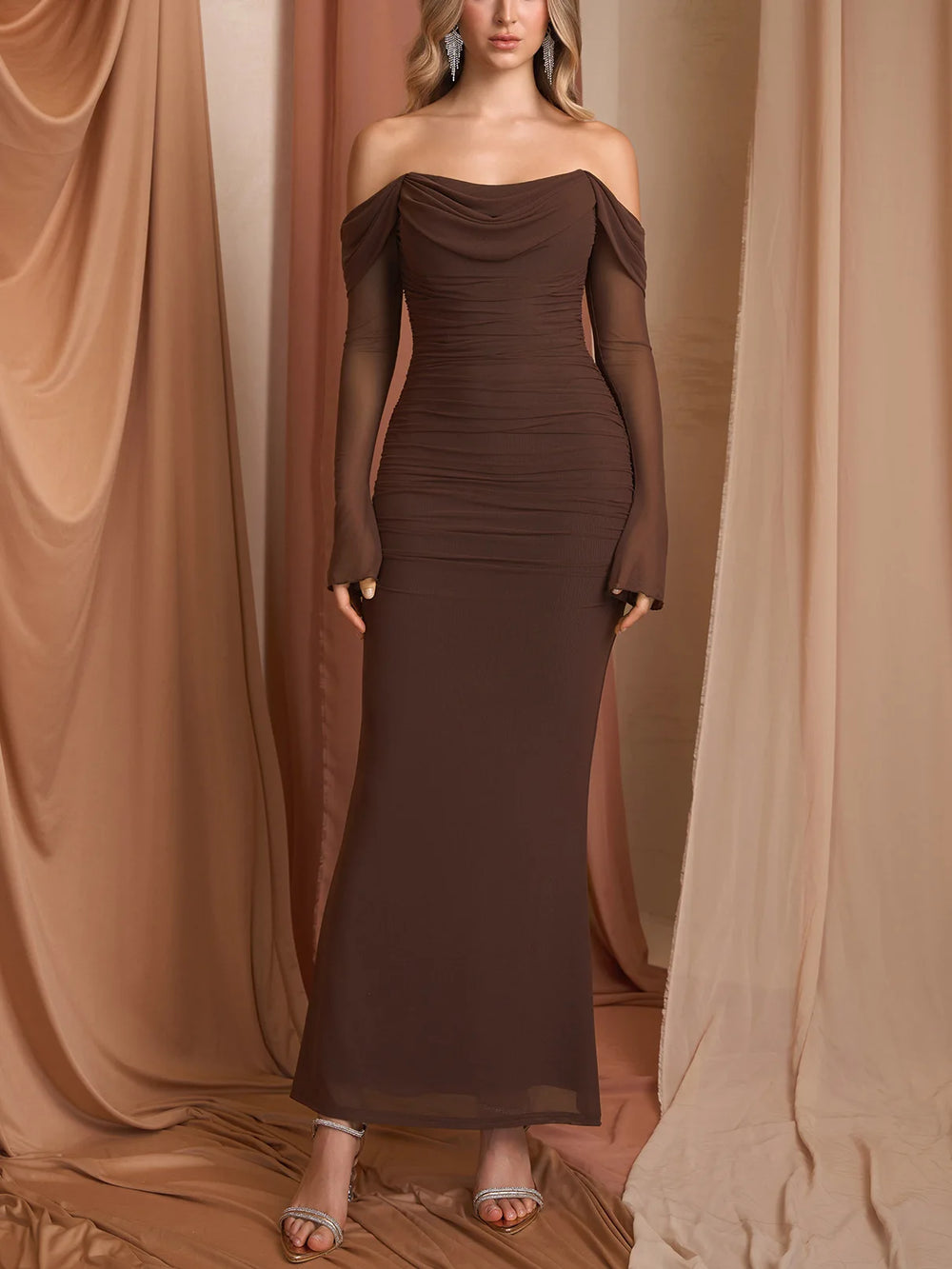 Woman wearing a brown off-shoulder evening gown against a draped curtain background