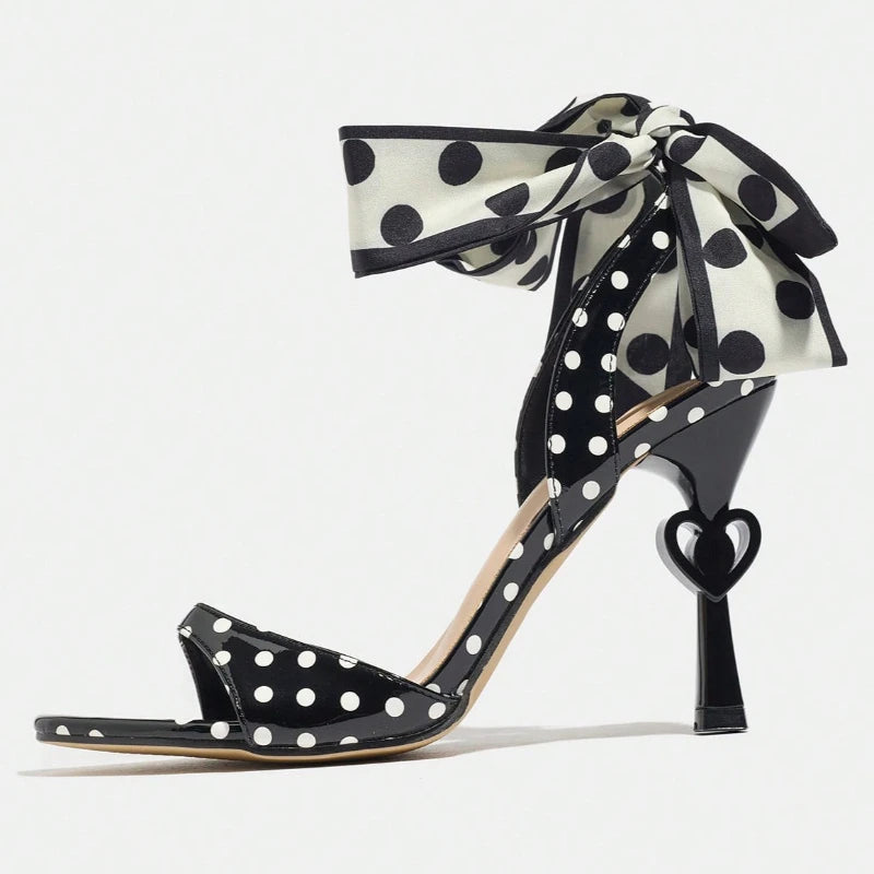 Black high-heeled shoe with white polka dots and a large bow on a white background