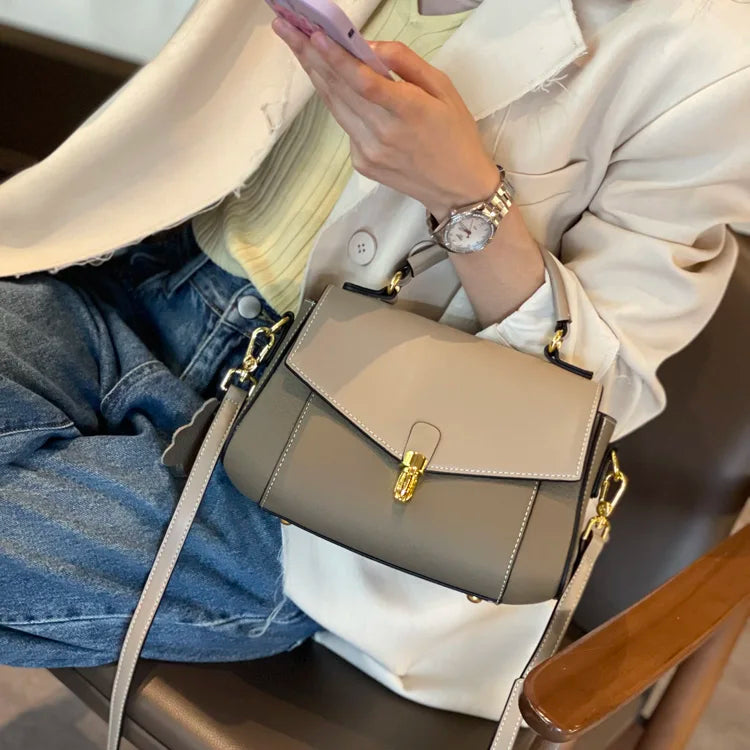 Person holding a beige handbag with a smartphone, wearing a white jacket and blue jeans.