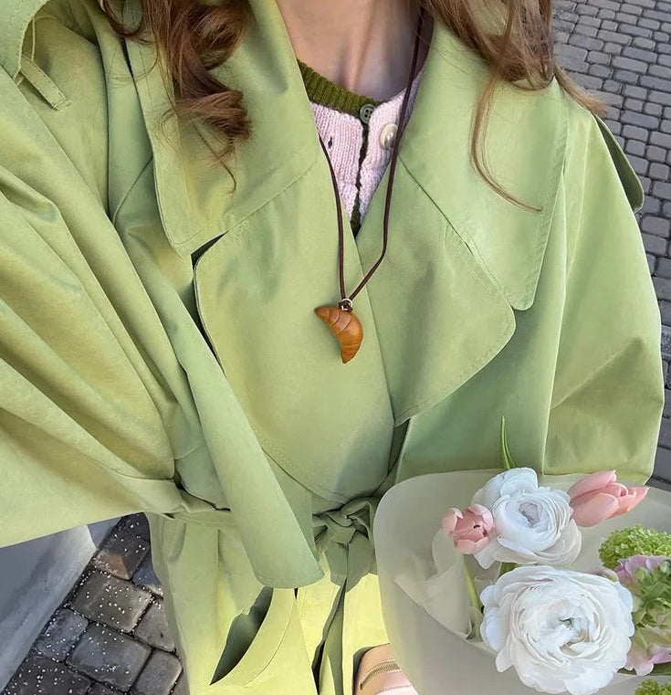 Person wearing a light green raincoat holding flowers on a cobbled street.