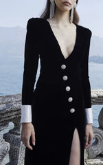 Black dress with silver buttons and a high slit worn by a model against a scenic background.