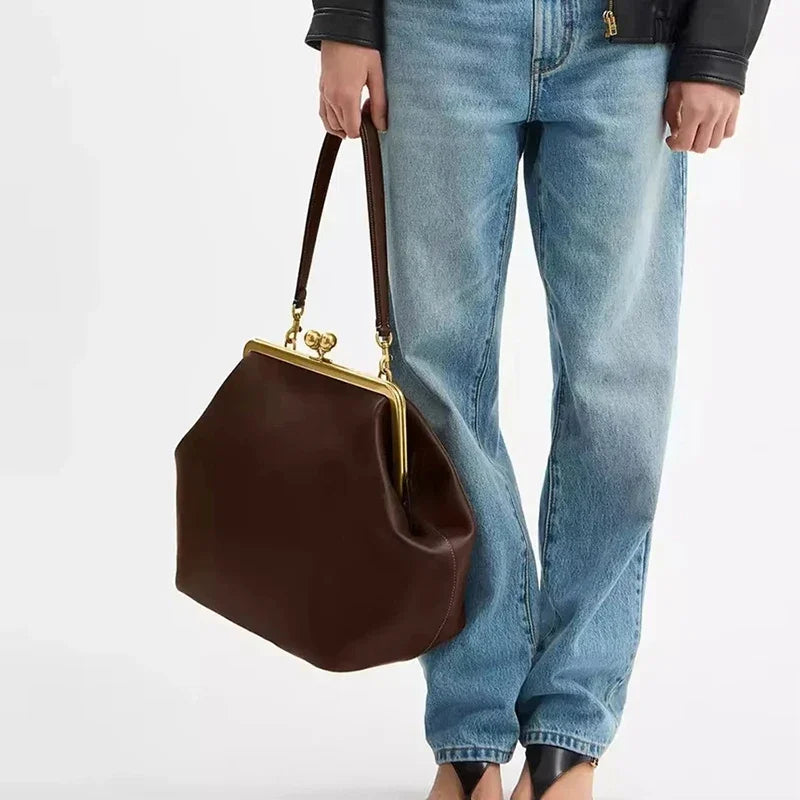 Brown handbag held by a person wearing blue jeans on a white background
