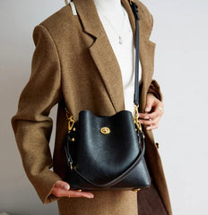 Person holding a black handbag with a gold clasp against a neutral background