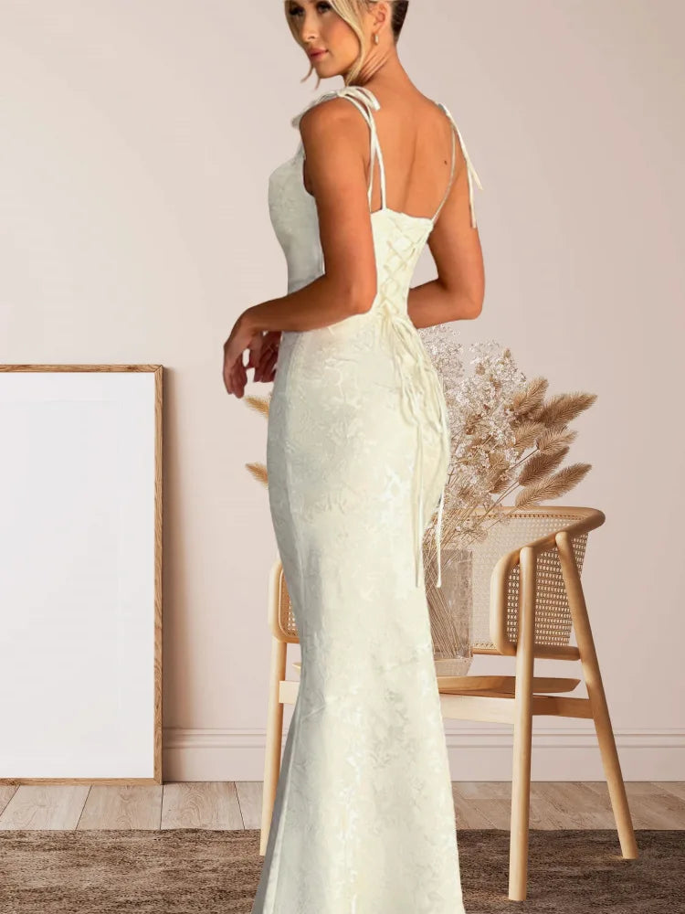 Woman in a light green lace dress standing in a room with a wooden chair and decorative plant.