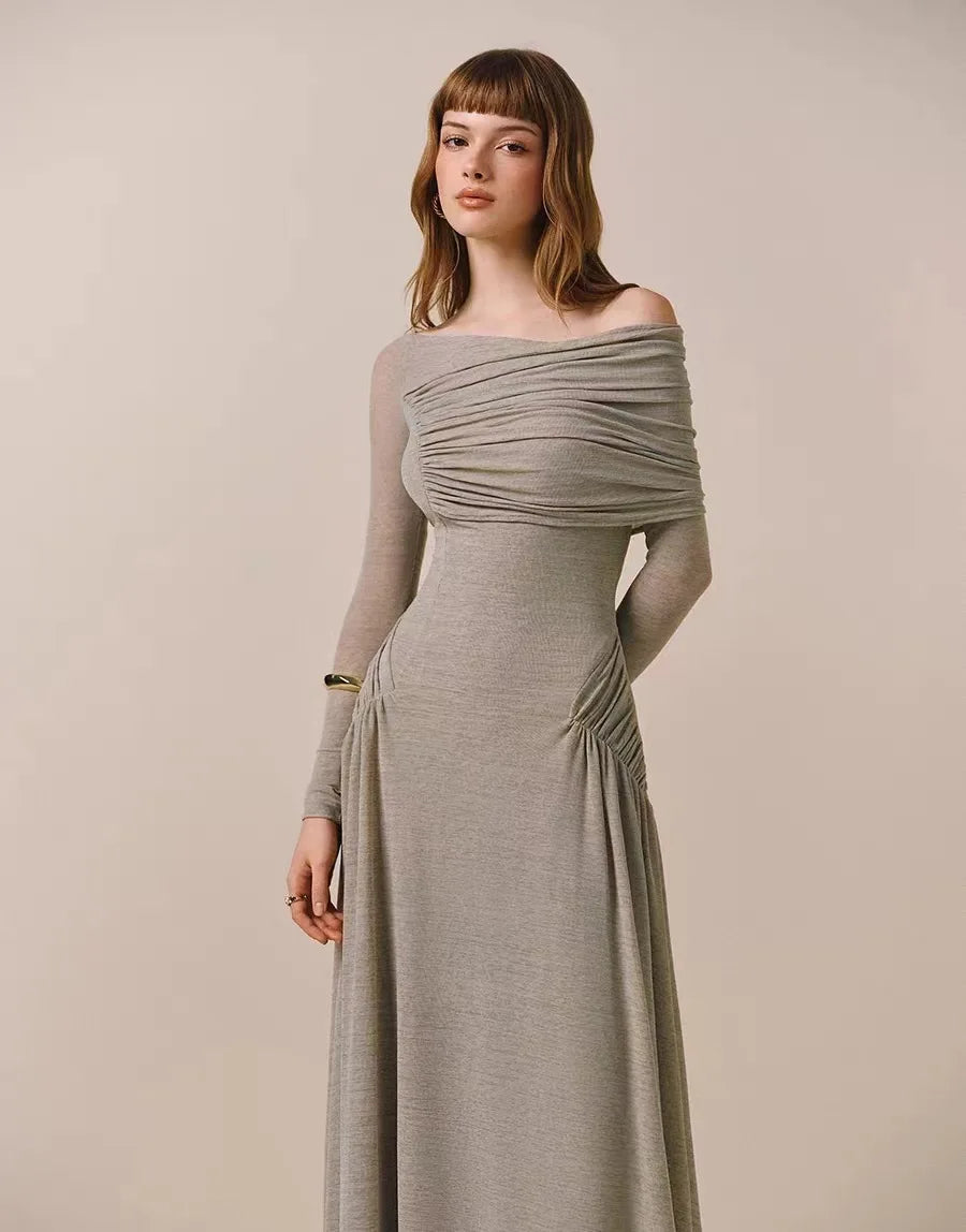 Woman wearing a long, off-shoulder gray dress against a plain background