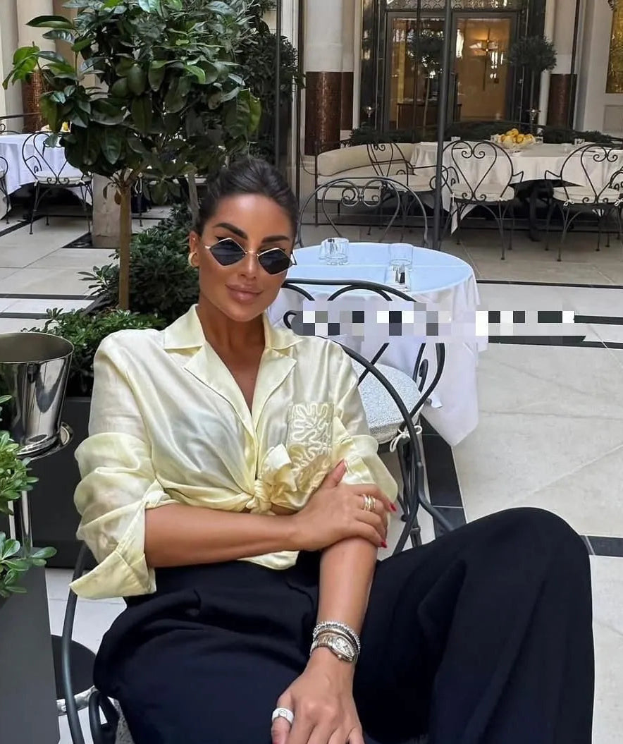 Woman sitting outdoors in a stylish setting with plants and tables in the background