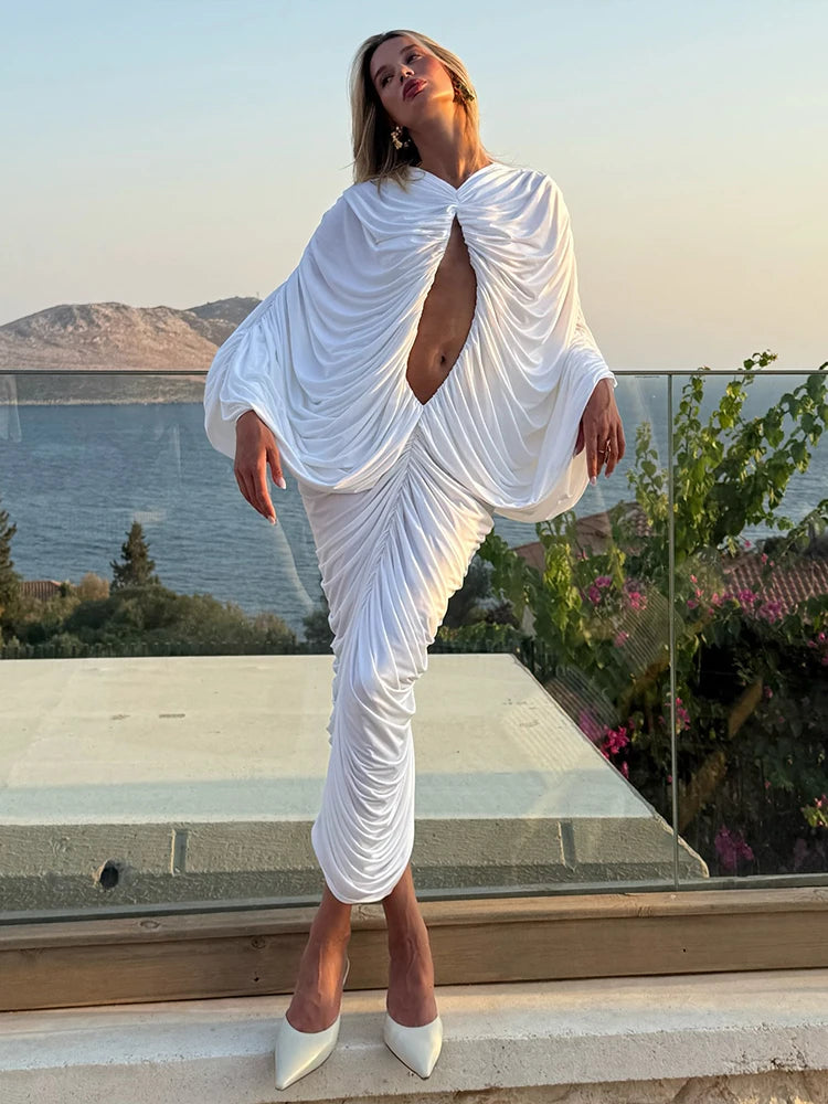 Woman in a white dress standing on a balcony with a scenic view of mountains and water.