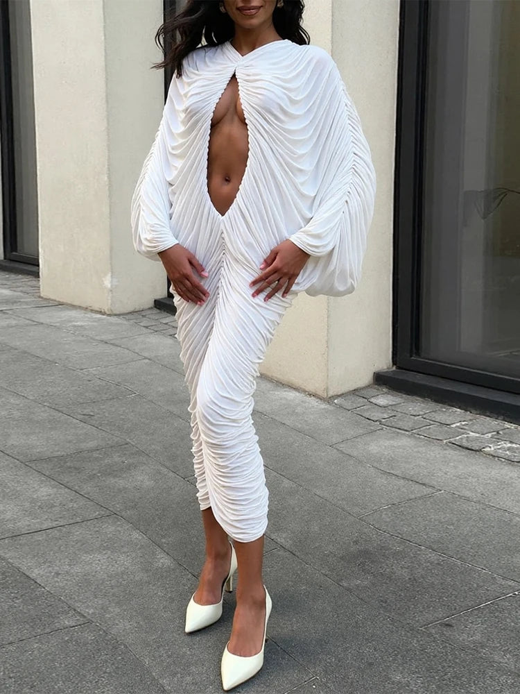 Woman wearing a white, ruched dress with a high slit on a city street.
