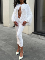 Woman wearing a white, ruched dress with a high slit on a city street.