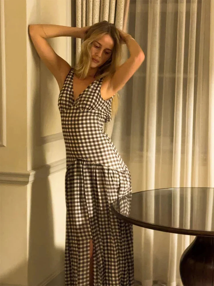 Woman in a checkered dress standing in a room with curtains and a table.