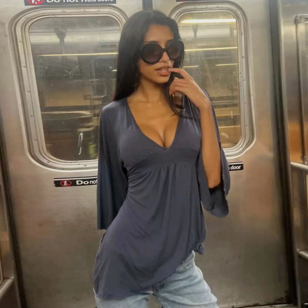 Woman in a gray top and jeans standing inside a subway car.