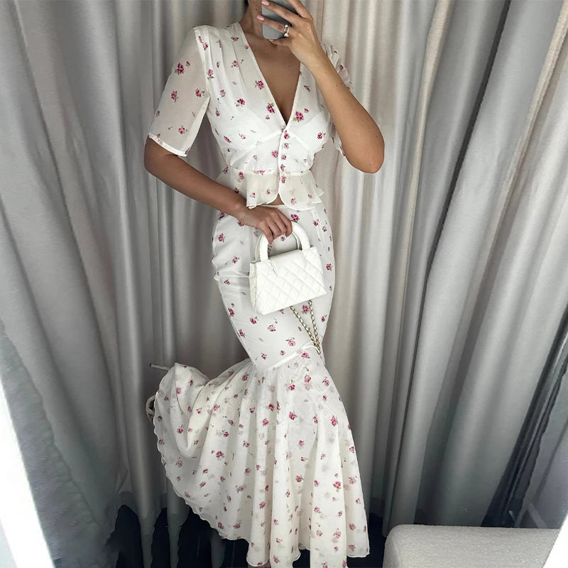 Person wearing a white floral dress holding a matching handbag against a neutral background