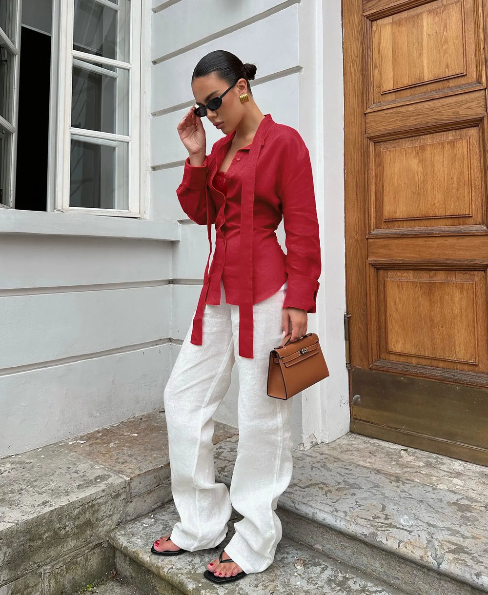 Woman in red blouse and white pants standing on steps outside a building.