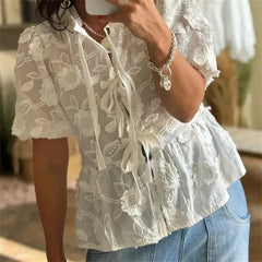 Person wearing a white lace blouse with floral patterns and blue jeans.