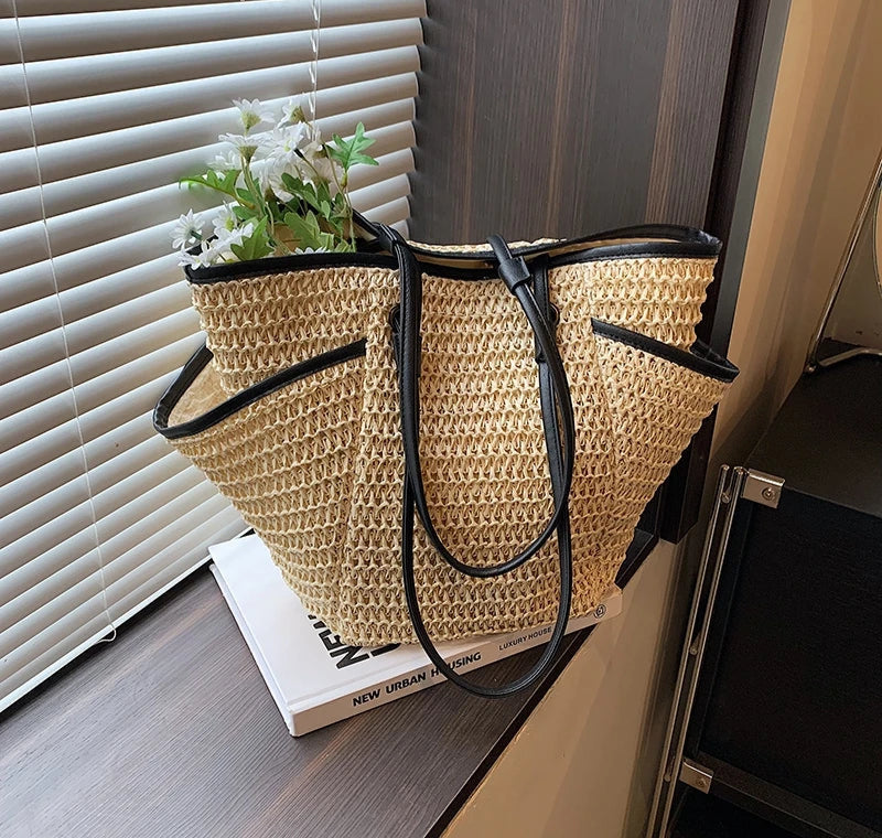 Woven straw bag with black handles on a surface near a window