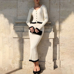 Woman in a white ribbed dress with black trim standing against a stone wall.