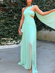 Woman wearing a light blue dress with a slit, standing outdoors against a green leafy background.
