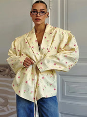Woman wearing a light yellow floral blouse with blue jeans against a neutral background