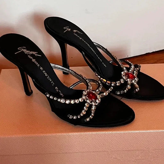 Side view of black open-toe stiletto heels with red spider gem embellishments.