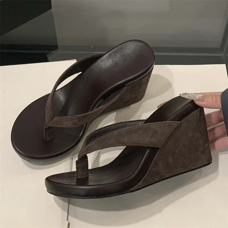 Brown wedge sandals on a white surface with a hand holding one sandal.