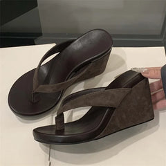 Brown wedge sandals on a white surface with a hand holding one sandal.