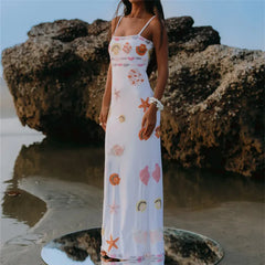 Woman in a white dress with starfish patterns standing on a rocky beach.