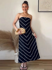 Woman wearing a strapless navy dress with white stripes, holding a woven bag indoors.