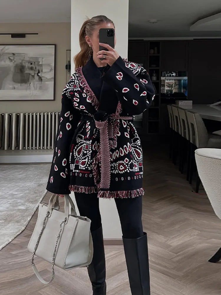 Person wearing a patterned coat and holding a white handbag indoors.