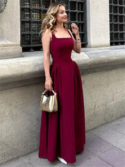Woman in a burgundy dress holding a gold handbag against a stone wall.