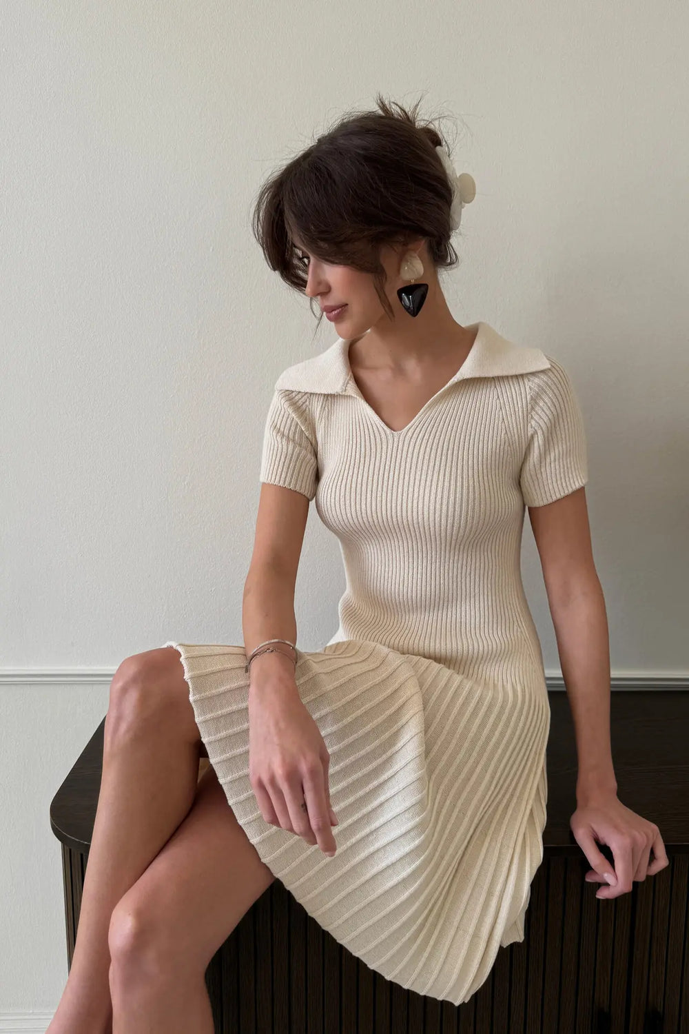 Woman wearing a beige dress sitting on a chair against a plain background