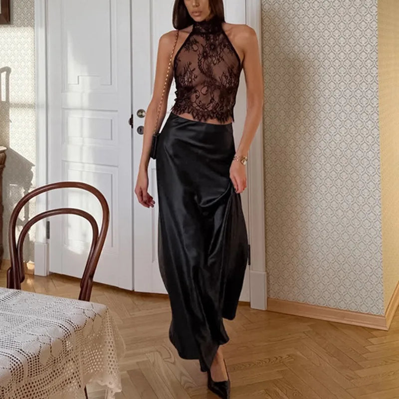 Woman in a black lace top and satin skirt standing in a room with wooden floor and white door.