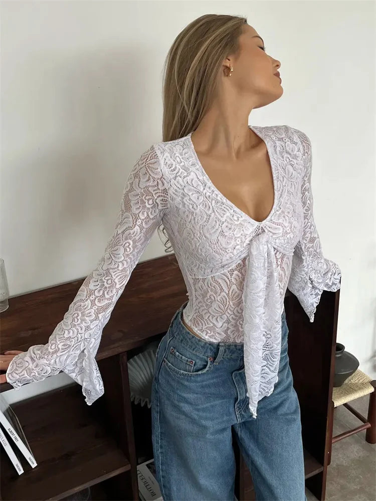 Woman wearing a white lace top and blue jeans in a room with wooden furniture.