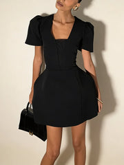 Woman wearing a black dress with puff sleeves against a beige background
