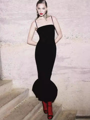 Woman in a black evening gown with a red lip standing on stone steps.