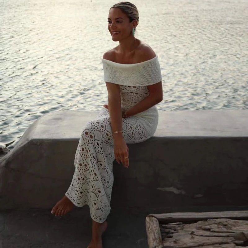 Woman in a white crochet outfit sitting by a body of water.