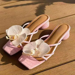 Pink high-heeled shoes with white orchids on a wooden surface