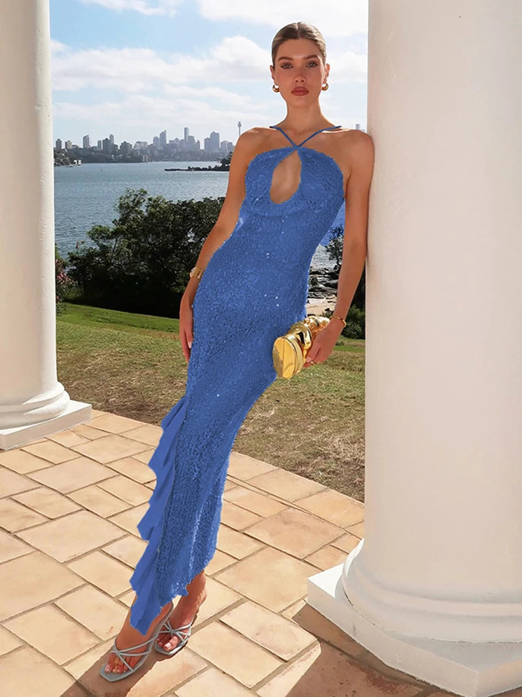 Woman in a blue sequin dress holding a yellow clutch by a waterfront with columns in the foreground.