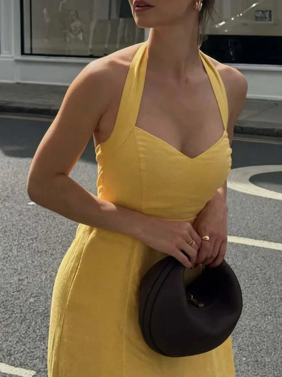 Woman in a yellow dress holding a black clutch on a street.
