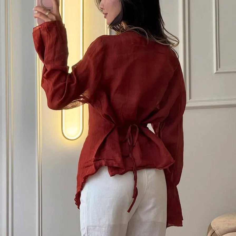 Person wearing a red blouse and white pants in a room with neutral walls.