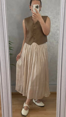 Person wearing a brown vest over a beige dress, standing in front of a mirror.