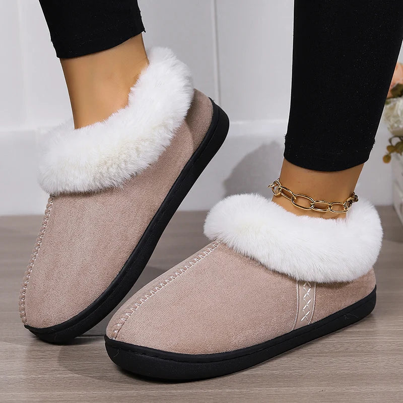 Beige slippers with white fur trim worn by a person on a wooden floor.