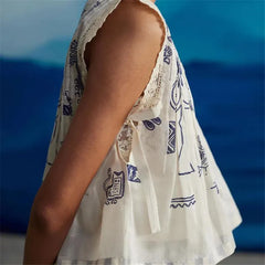 White sleeveless top with blue patterns against a blurred blue background