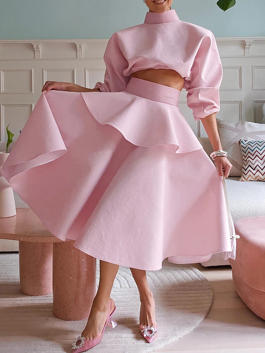 Person wearing a pink two-piece outfit with a skirt and cropped top in a room.