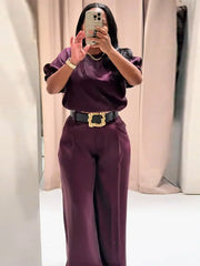 Person wearing a purple outfit with a gold belt in front of beige curtains