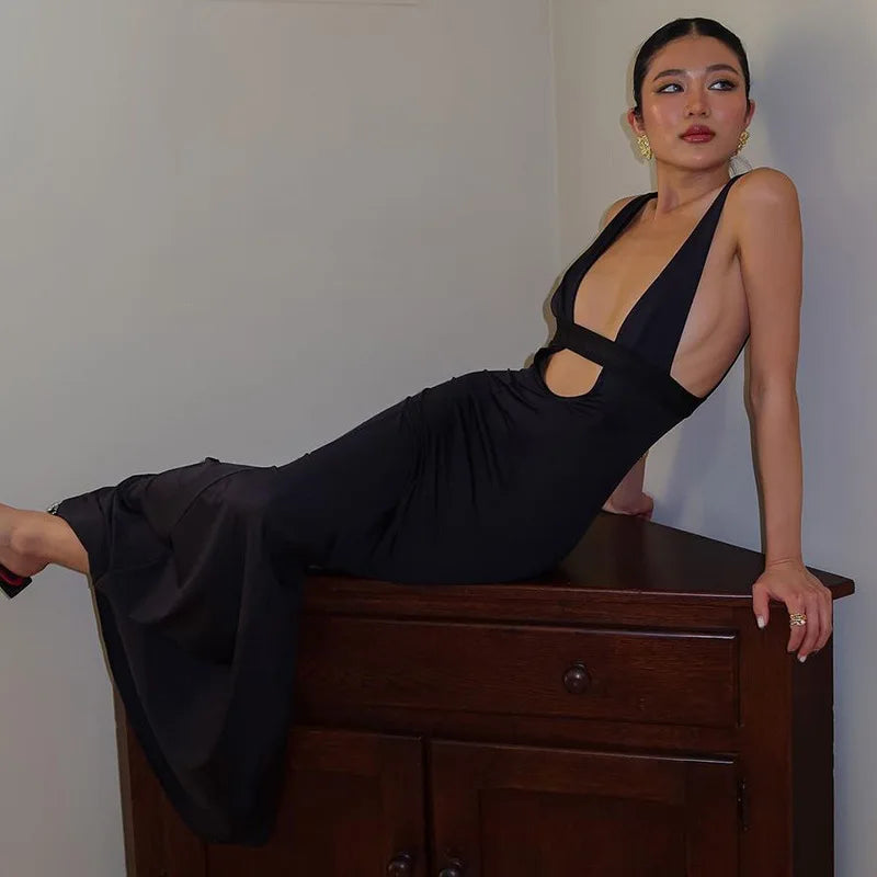 Woman in a black dress posing on a wooden dresser against a plain wall.