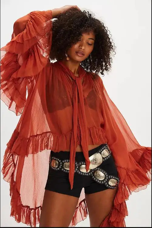 Woman wearing a red sheer jacket over a black outfit with white embellishments on a white background