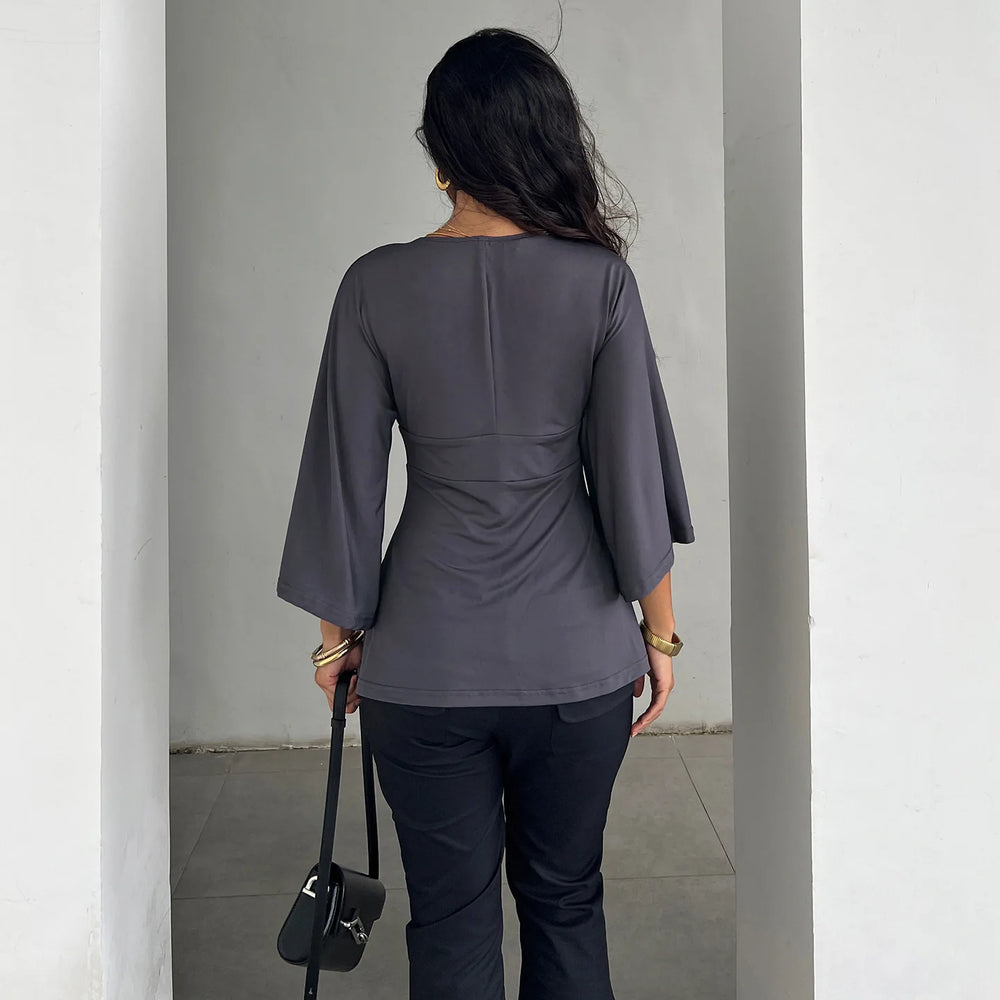 Person wearing a gray top and black pants against a plain background